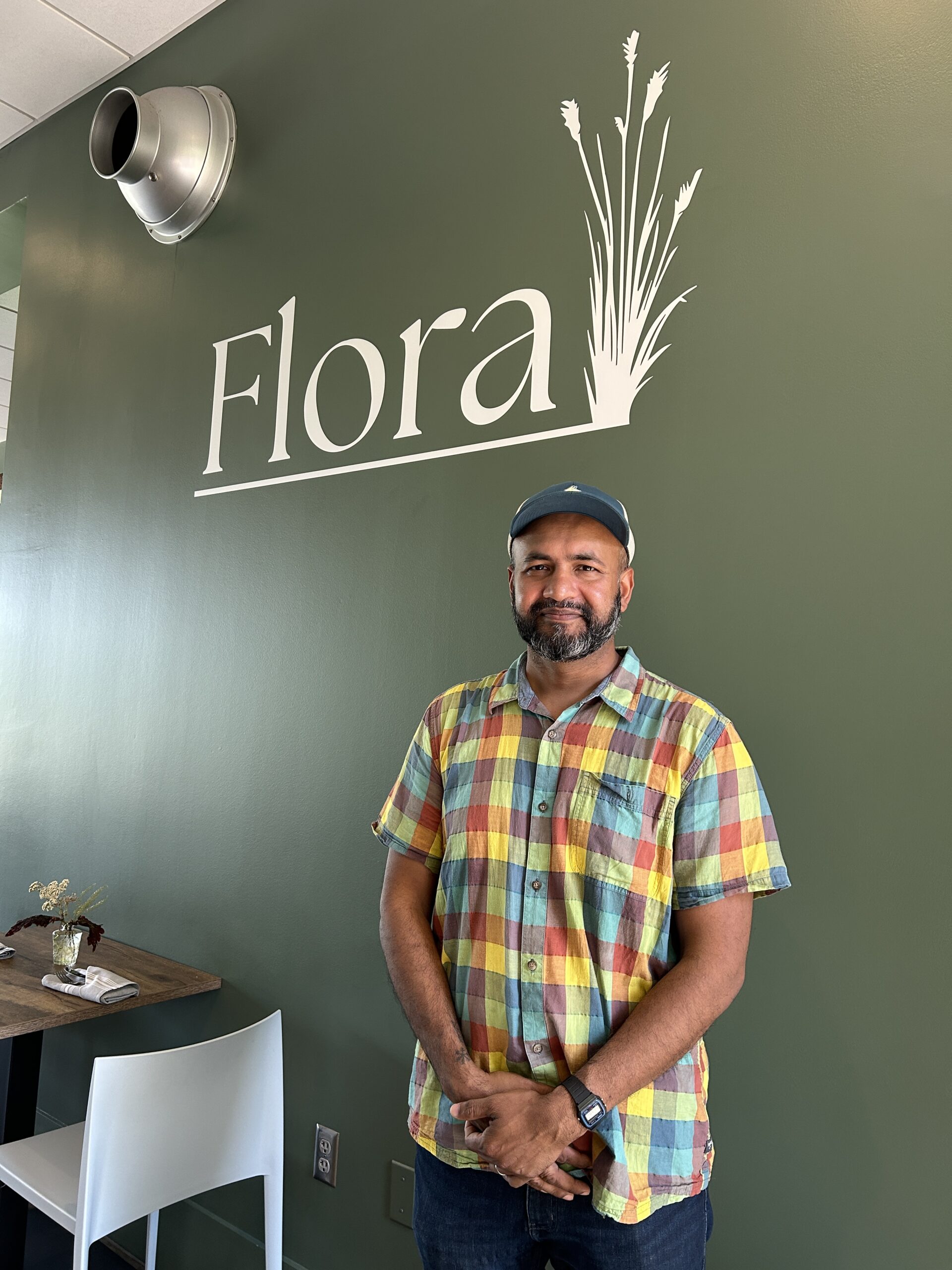 suman hoque standing in front of a sign with the name of his restaurant, Flora