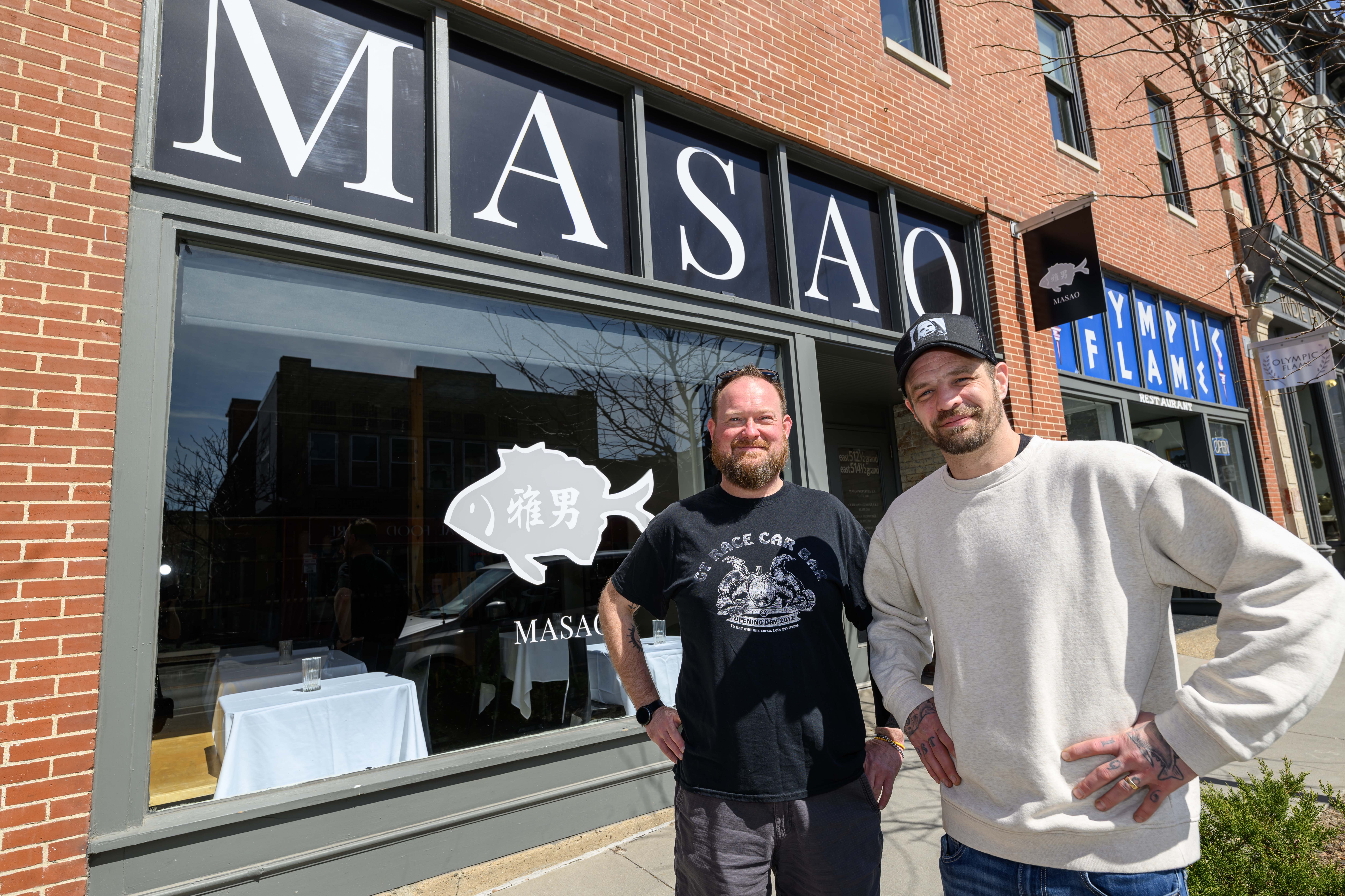 Nick Hanke and Phil Shires stand in front of a glass window with Masao's name and fish logo printed across.